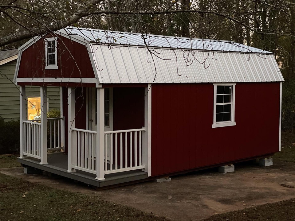 A shed with red siding and white roof and porch by Liberty Sheds.